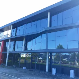 Nowoczesny budynek biurowy z dużą ilością szklanych okien odbijających otoczenie, widoczny znak firmy 'WB TRIM TECH' na elewacji.