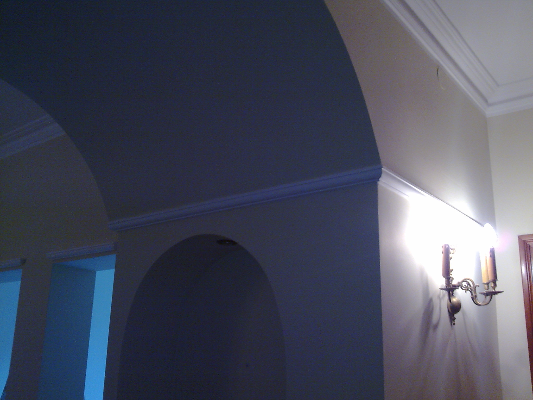 Łukowe przejście między pomieszczeniami z ozdobnymi listwami sufitowymi i kinkietem w stylu retro