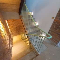 Andrzej Mazelon Usługi Spawalnicze - Betonowe schody z jasnozieloną poręczą w Świerzawie, oświetlone punktowymi lampami. Ceglana ściana z boku dodaje surowego charakteru wnętrzu.