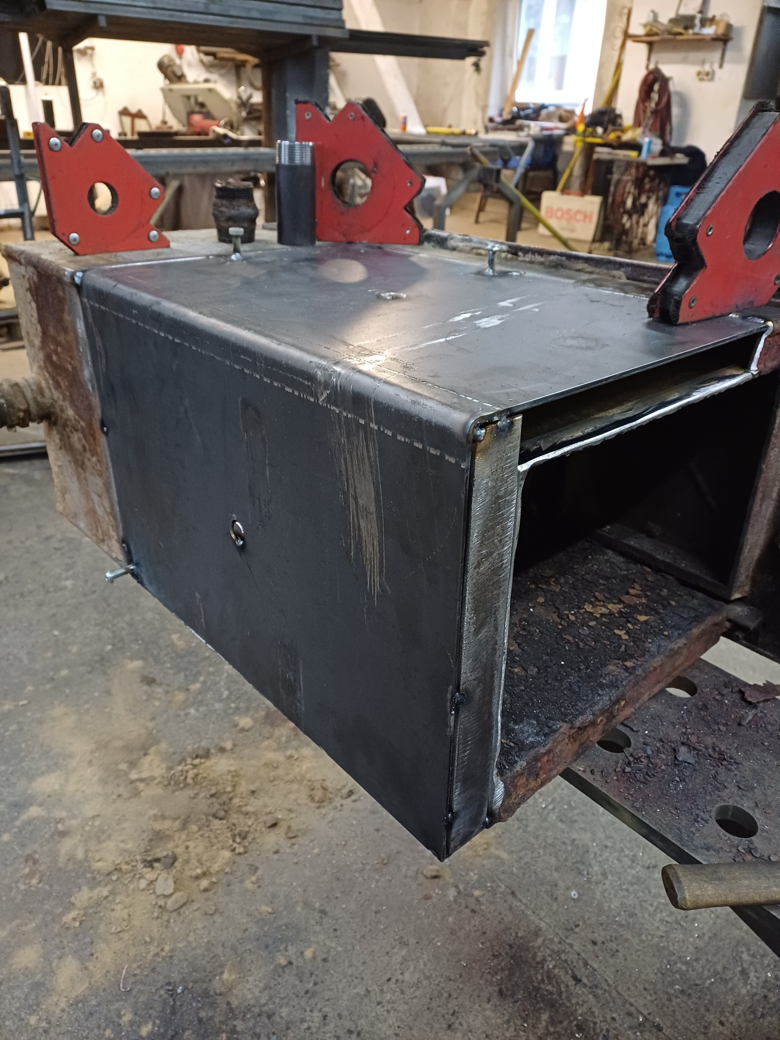 Metalowa konstrukcja spawana w warsztacie, z użyciem uchwytów magnetycznych, ukazująca etap prac spawalniczych. Widoczne ślady spawania i narzędzia.