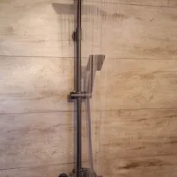 Nowoczesny, czarny zestaw prysznicowy z deszczownicą i słuchawką, zamontowany na ścianie wyłożonej panelami imitującymi drewno, w trakcie użytkowania.