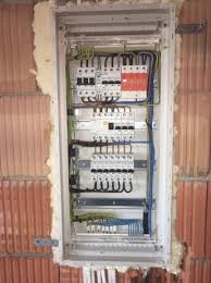 Rozdzielnica elektryczna w trakcie montażu, widoczne zabezpieczenia, przewody i elementy montażowe, ściana z pustaków ceramicznych z widoczną pianką montażową.