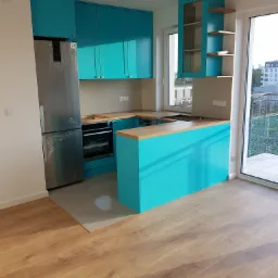 Nowoczesna kuchnia z turkusowymi szafkami i drewnianymi blatami, srebrna lodówka w folii ochronnej, widok z perspektywy podłogi z paneli.