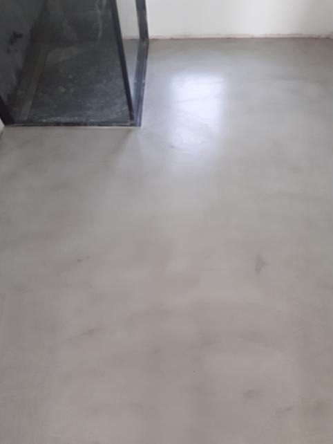 Jasnoszara, jednolita podłoga w łazience, widoczna kabina prysznicowa z czarną ramą, gładka powierzchnia z delikatnym połyskiem.