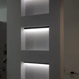 Trzy podświetlane wnęki w szarej ścianie, z czarnymi oprawami oświetleniowymi, tworzące minimalistyczny design.