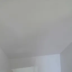 Biały sufit i ściany w rogu pokoju, widoczne delikatne przejścia światłocieni.