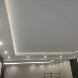 SF-Wykończenia Wnętrz (Quality) - Nowoczesne wykończenie sufitu z płyt karton gips z wbudowanym oświetleniem LED i punktowymi lampami, ściany pomalowane na szaro, widoczny fragment rusztowania.