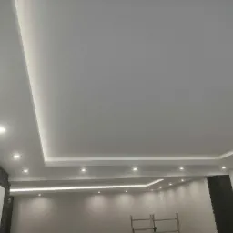 Nowoczesne wykończenie sufitu z płyt karton gips z wbudowanym oświetleniem LED i punktowymi lampami, ściany pomalowane na szaro, widoczny fragment rusztowania.