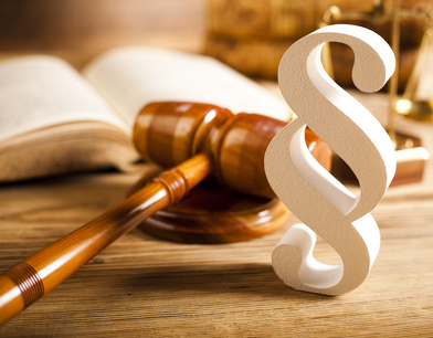 Symbol paragrafu z drewnianym młotkiem sędziowskim, otwartą książką i wagą na drewnianym biurku, ciepłe oświetlenie.