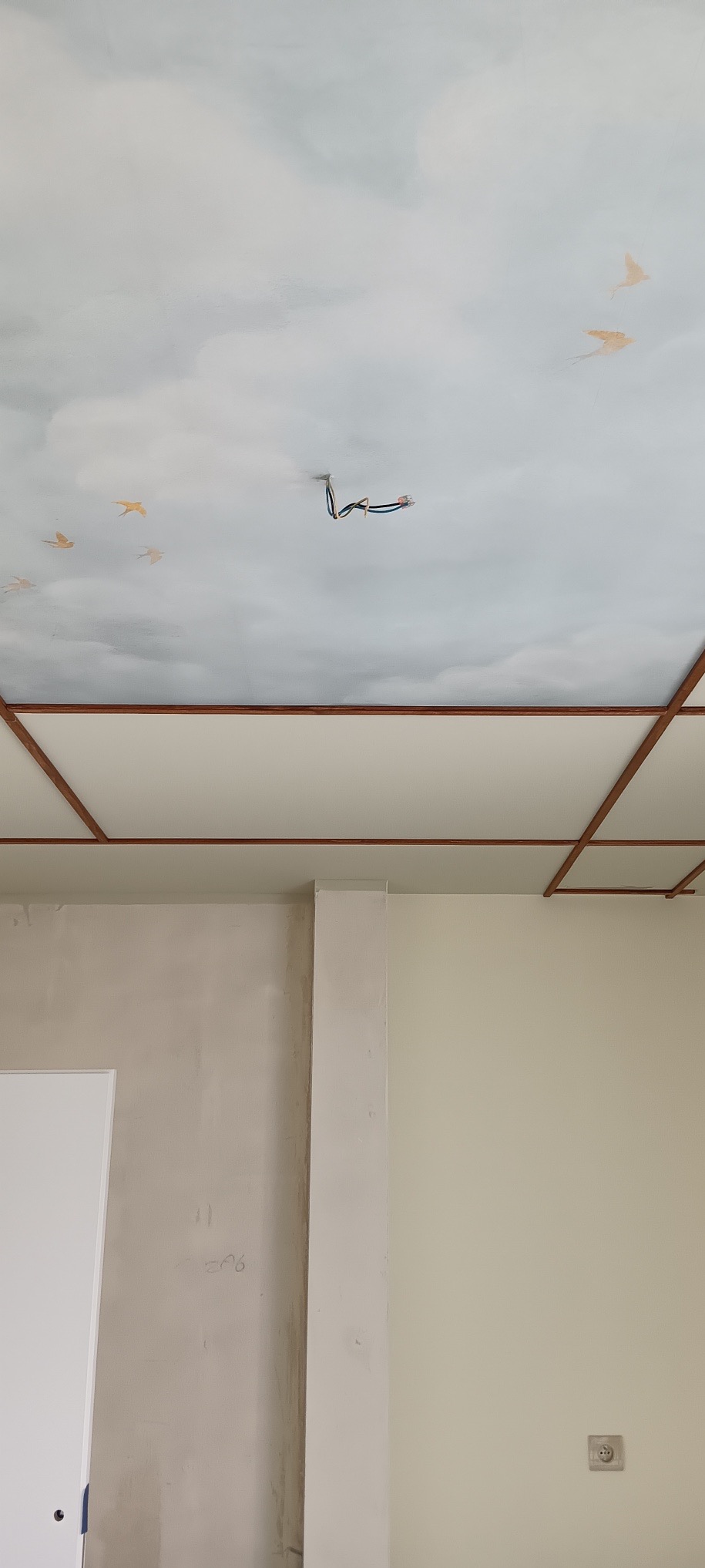 Malowany sufit z motywem nieba i ptaków w trakcie wykańczania wnętrza. Widoczne przewody elektryczne i fragmenty ścian w jasnych odcieniach.