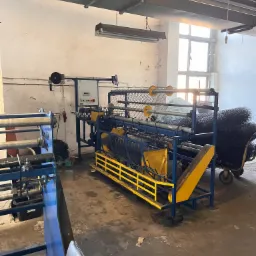 Maszyna do produkcji siatki ogrodzeniowej w hali produkcyjnej w Ornecie, z widoczną rolką gotowej siatki na wózku.