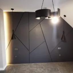 Nowoczesna ściana z płyt karton gips z geometrycznym wzorem i oświetleniem LED, uzupełniona wiszącymi lampami w kolorze czarnym