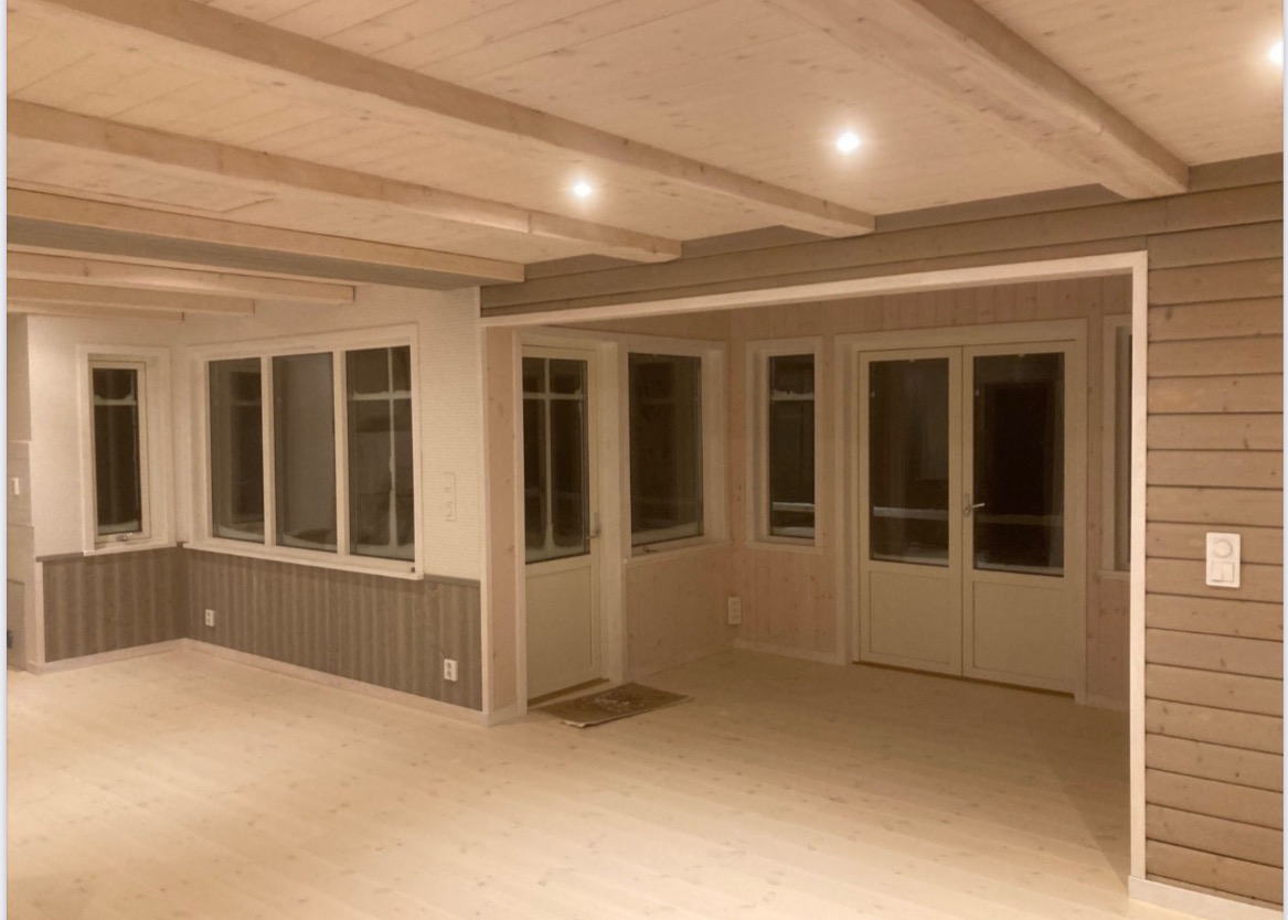 Jasne, drewniane wnętrze domu z oknami i drzwiami, wykończone w naturalnym stylu, widoczne listwy i belki stropowe, oświetlenie punktowe.