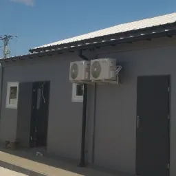 Dwa klimatyzatory zamontowane na szarej ścianie budynku z blachy trapezowej, widoczne rynny i instalacja elektryczna na dachu