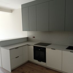 WOPREM - Nowoczesna kuchnia z szarymi szafkami górnymi i białymi dolnymi, drewniana podłoga. Minimalistyczny design, czarne uchwyty, płyta indukcyjna. Oświetlenie sufitowe.