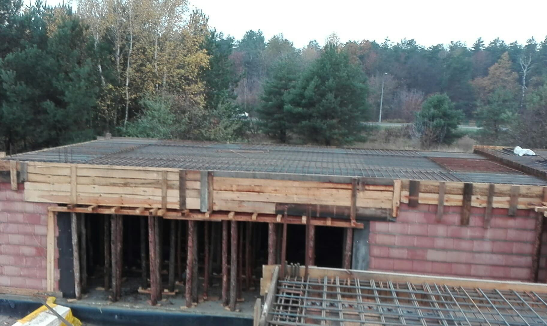 Wykonywanie stropu żelbetowego: szalunek z desek, stalowe zbrojenie i podpory pionowe, w tle las.