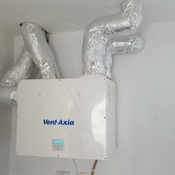 PANEA - Centrala wentylacyjna Vent-Axia zamontowana na ścianie z podłączonymi przewodami wentylacyjnymi w izolacji aluminiowej.