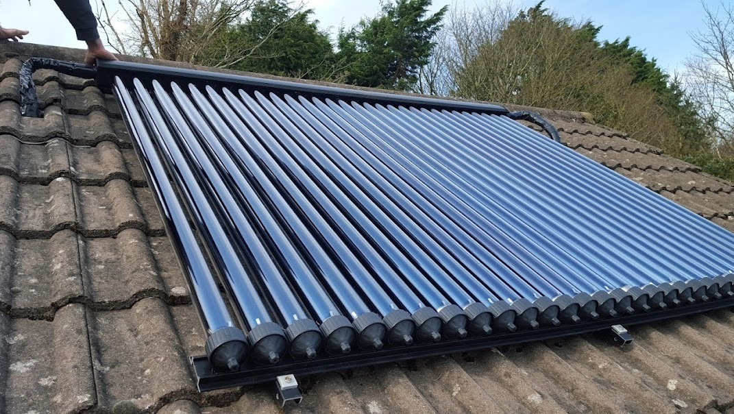 Panel solarny z rur próżniowych zamontowany na dachu pokrytym starą dachówką, widoczne połączenia rur i elementy mocujące.