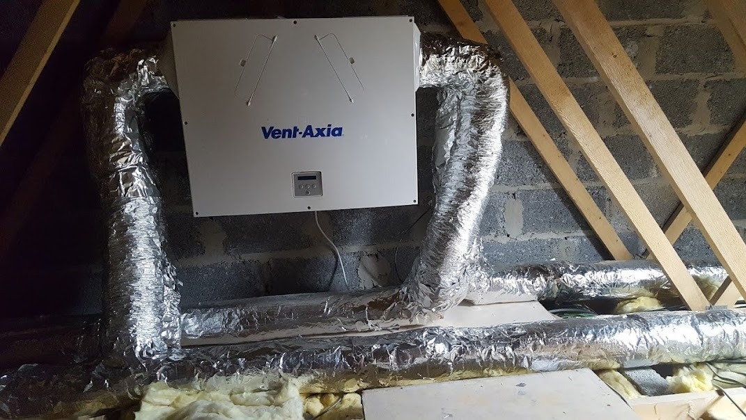 Centrala wentylacyjna Vent-Axia z aluminiowymi przewodami w szarej przestrzeni poddasza w Kamionnej, widoczne elementy konstrukcji drewnianej dachu.