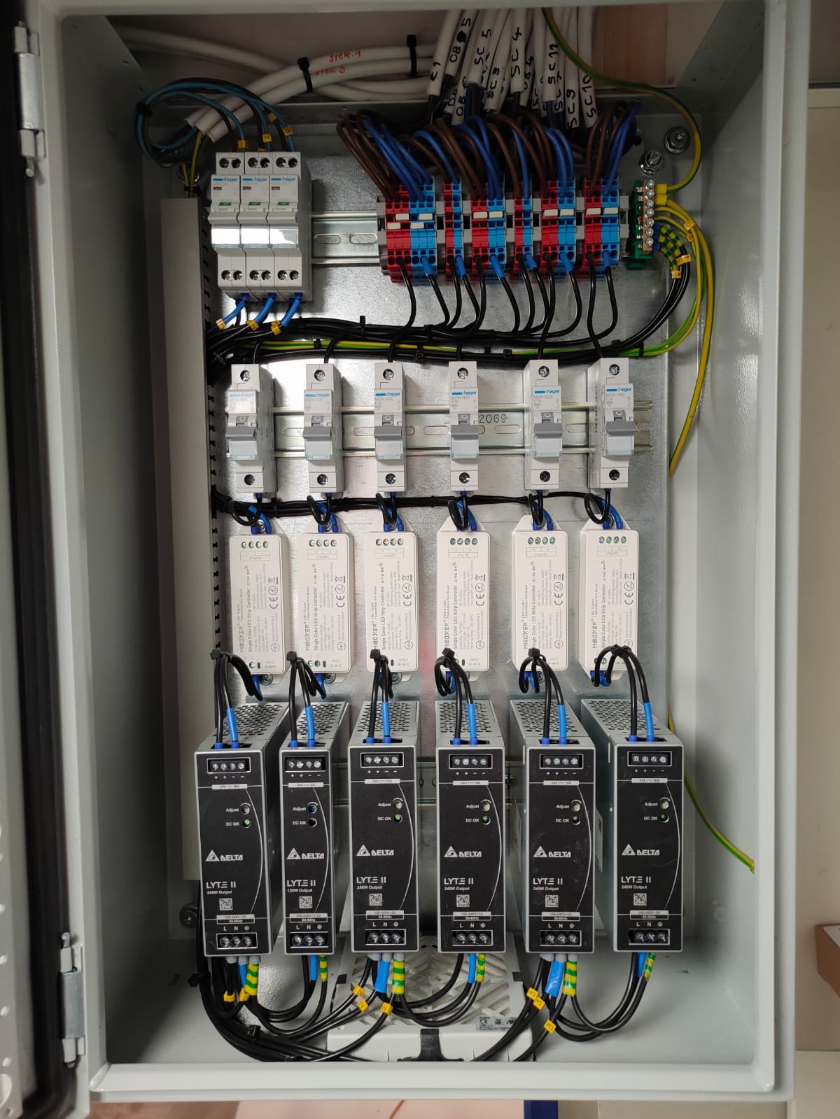 Wnętrze skrzynki elektrycznej z zamontowanymi bezpiecznikami, złączkami i sterownikami LED, starannie połączonymi przewodami w różnych kolorach, widoczne oznaczenia na przewodach i urządzeniach.