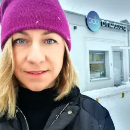 Portret kobiety w fioletowej czapce na tle budynku szkoły językowej w zimowej scenerii w Grudziądzu. Widoczne logo firmy na budynku.