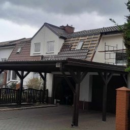 Solid-Dach - Wymiana dachu w trakcie: widoczne drewniane łaty i częściowo położona brązowa dachówka na dwuspadowym dachu domu jednorodzinnego z podjazdem.