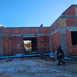 Solid-Dach - Surowy stan budynku z czerwonej cegły z widocznym rusztowaniem i pracownikami na zewnątrz w słoneczny dzień.