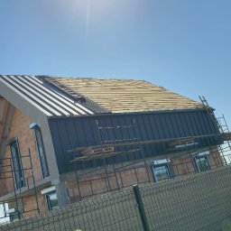 Solid-Dach - Wymiana dachu w trakcie: widok na dom w budowie z częściowo zdjętym starym pokryciem i zamontowaną blachą na części dachu, rusztowania dookoła budynku.