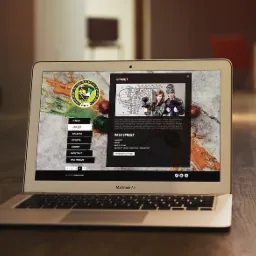Laptop MacBook Air wyświetla stronę internetową z motywem paintballowym, z logo firmy i zdjęciem graczy w sprzęcie, na drewnianym stole.
