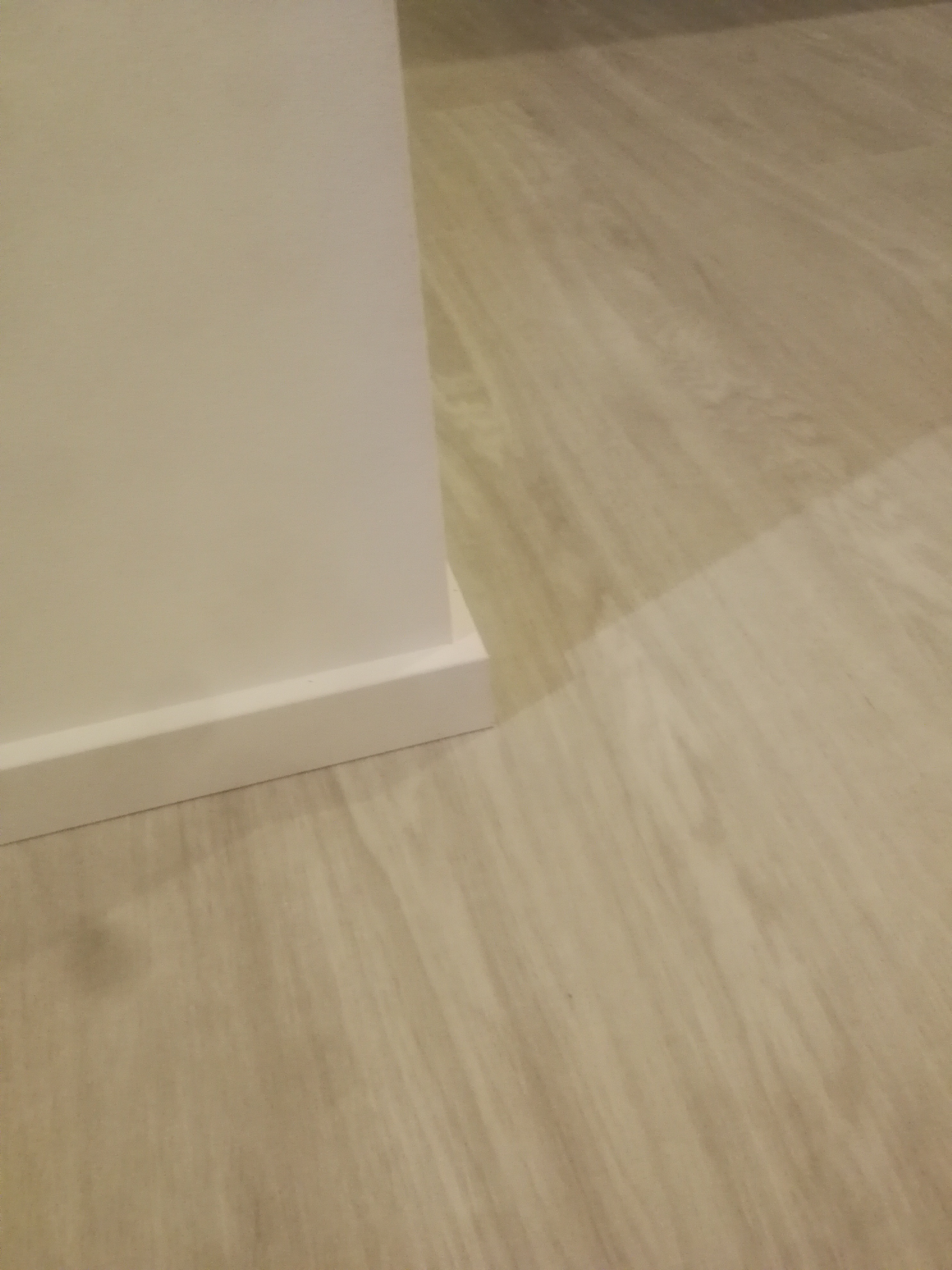 Fragment ściany z przypodłogową listwą oraz panele podłogowe w odcieniach beżu, widoczne pod kątem.