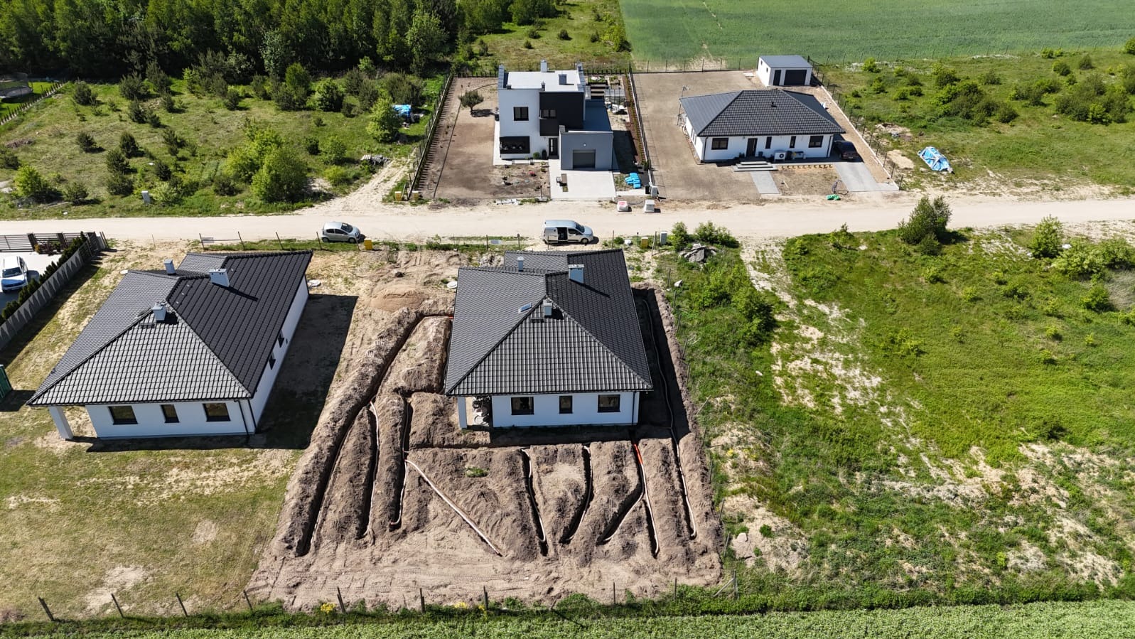 Nowy dom z instalacją podziemną w wykopach, widok z lotu ptaka, sąsiednie domy w tle.