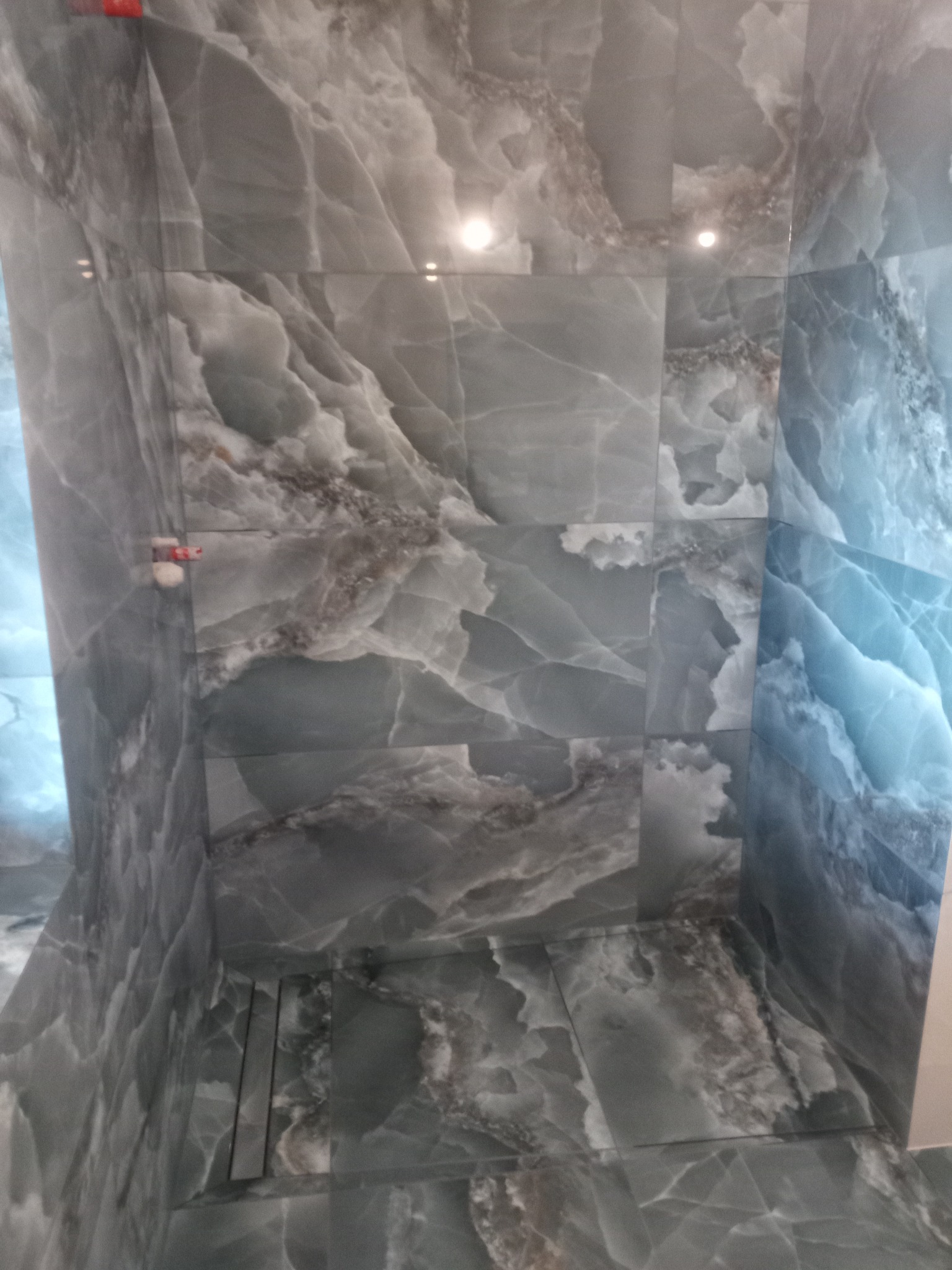 Wykończona kabina prysznicowa z szarymi płytkami imitującymi marmur, widoczny odpływ liniowy w podłodze.