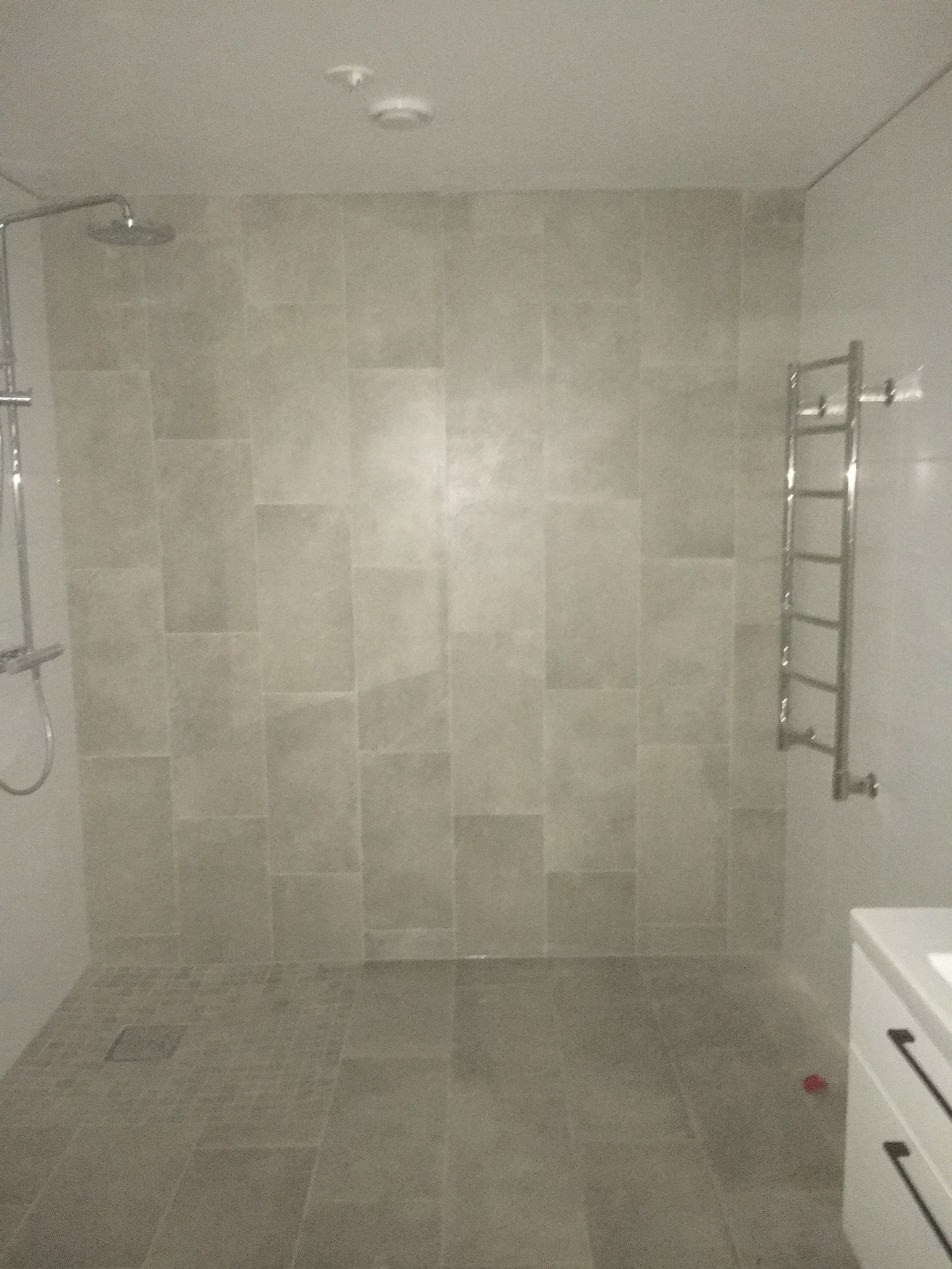 Nowoczesna kabina prysznicowa walk-in z szarymi płytkami w Gdańsku, z odpływem liniowym i grzejnikiem drabinkowym.