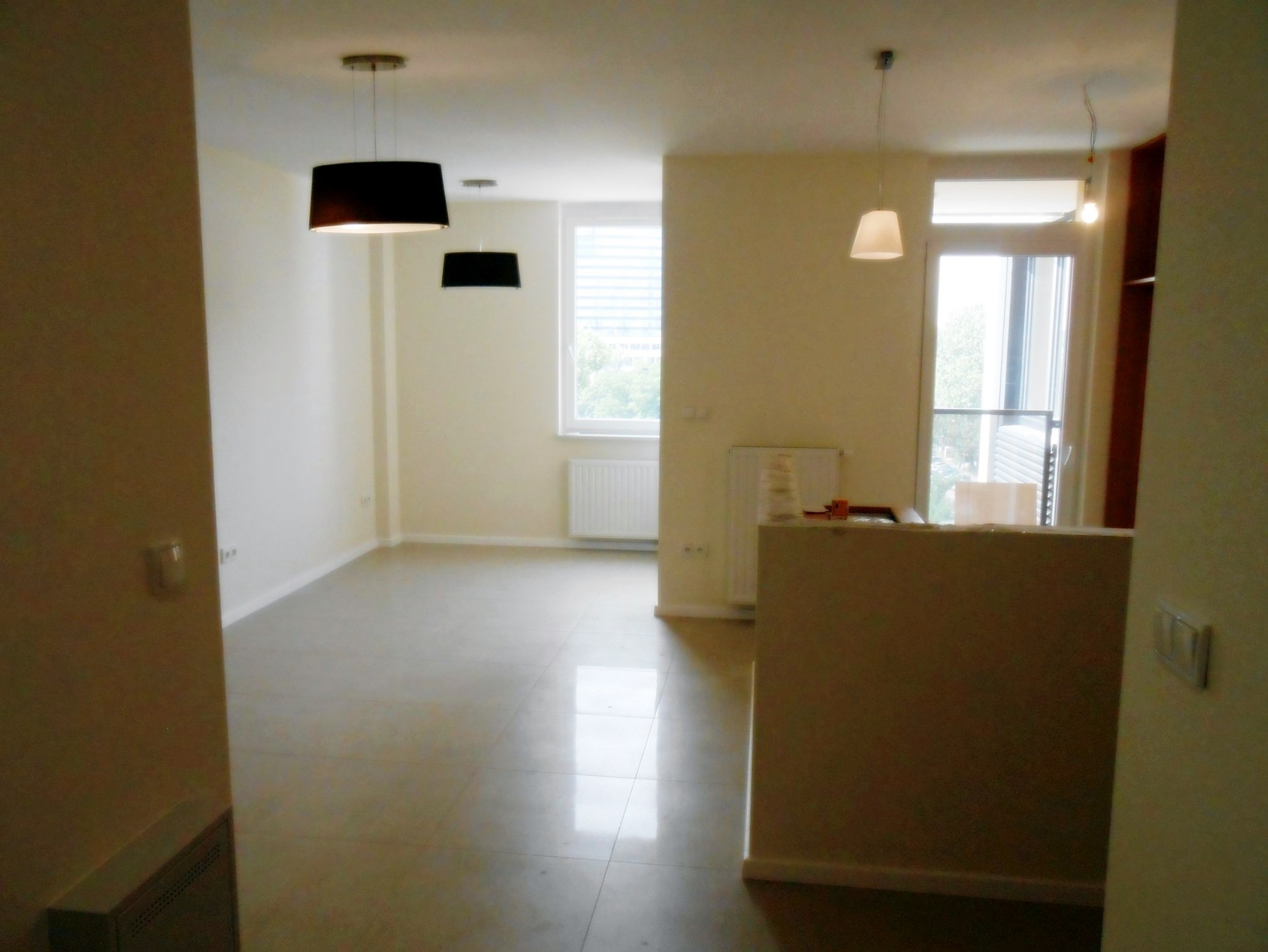 Jasne, przestronne wnętrze po remoncie z trzema nowoczesnymi lampami wiszącymi, białymi ścianami i błyszczącą, jasną podłogą z płytek.