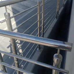 Błyszcząca, metalowa balustrada ze stali nierdzewnej na schodach zewnętrznych, z widocznymi odbiciami światła na gładkiej powierzchni poręczy.