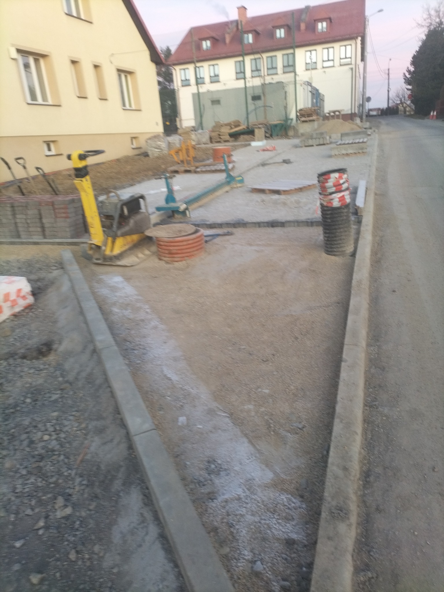 Przygotowanie podłoża pod chodnik z kostki brukowej: ubijarka wibracyjna, krawężniki i materiały budowlane na placu budowy.