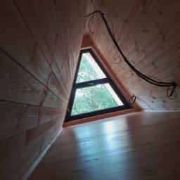 ART-BUD - Wnętrze poddasza wykończonego drewnem, z trójkątnym oknem wychodzącym na zewnątrz i widocznymi kablami elektrycznymi.