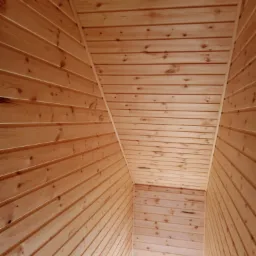 Wnętrze wykończone jasnymi panelami drewnianymi, widok z dołu na skośny sufit i ściany.