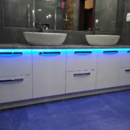 Nowoczesna łazienka z podświetlaną szafką pod umywalki nablatowe i szarym marmurem na ścianach.