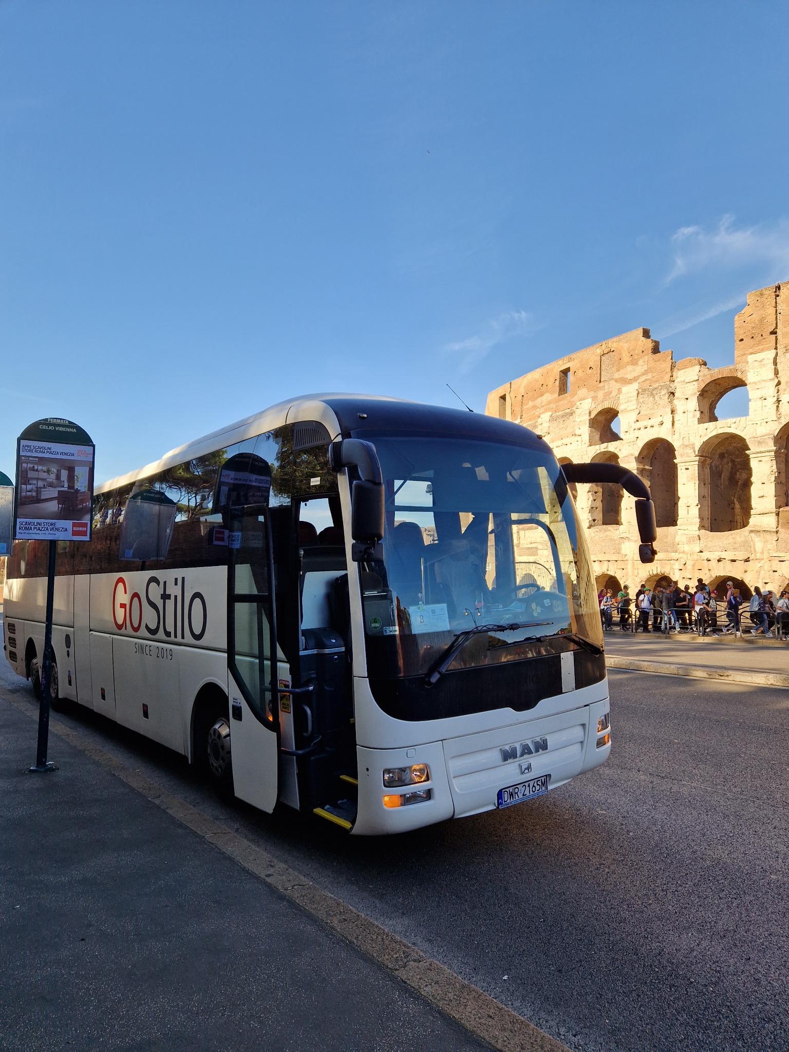 Autokar turystyczny GoStilo zaparkowany na tle Koloseum w Rzymie, otwarte drzwi wejściowe, widoczni turyści.