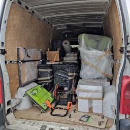 MoveTransport - Wnętrze białego furgonetki wypełnione po brzegi zapakowanymi przedmiotami, w tym meblami owiniętymi folią bąbelkową, kartonami i wózkiem transportowym w kolorze limonkowym.