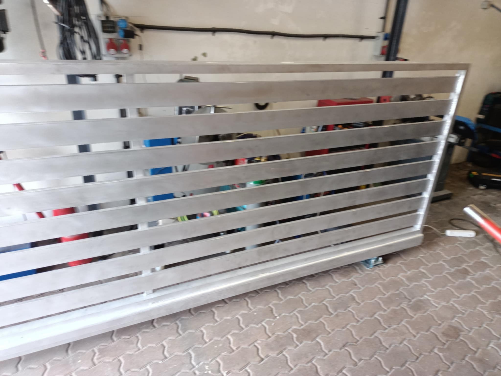 Metalowa brama przesuwna z poziomymi szczeblami, widoczna na kostce brukowej w warsztacie.