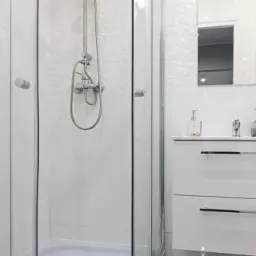 Nowoczesna, biała łazienka z kabiną prysznicową ze srebrnym zestawem natryskowym, umywalką z szafką i lustrem na ścianie pokrytej trójwymiarowymi płytkami.