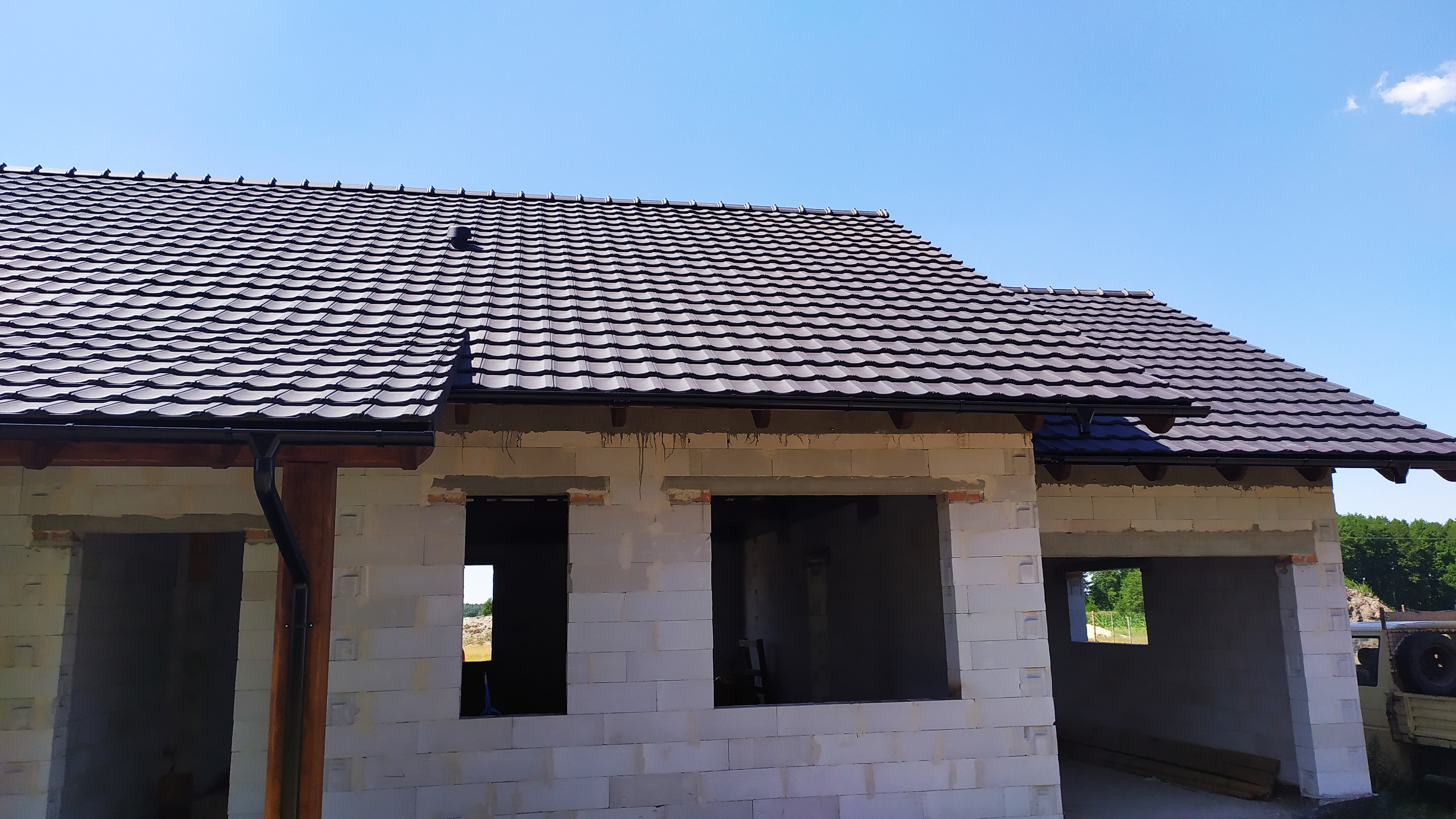 Nowy budynek w trakcie budowy z ciemną dachówką ceramiczną, widoczne rynny i niezamontowane okna.