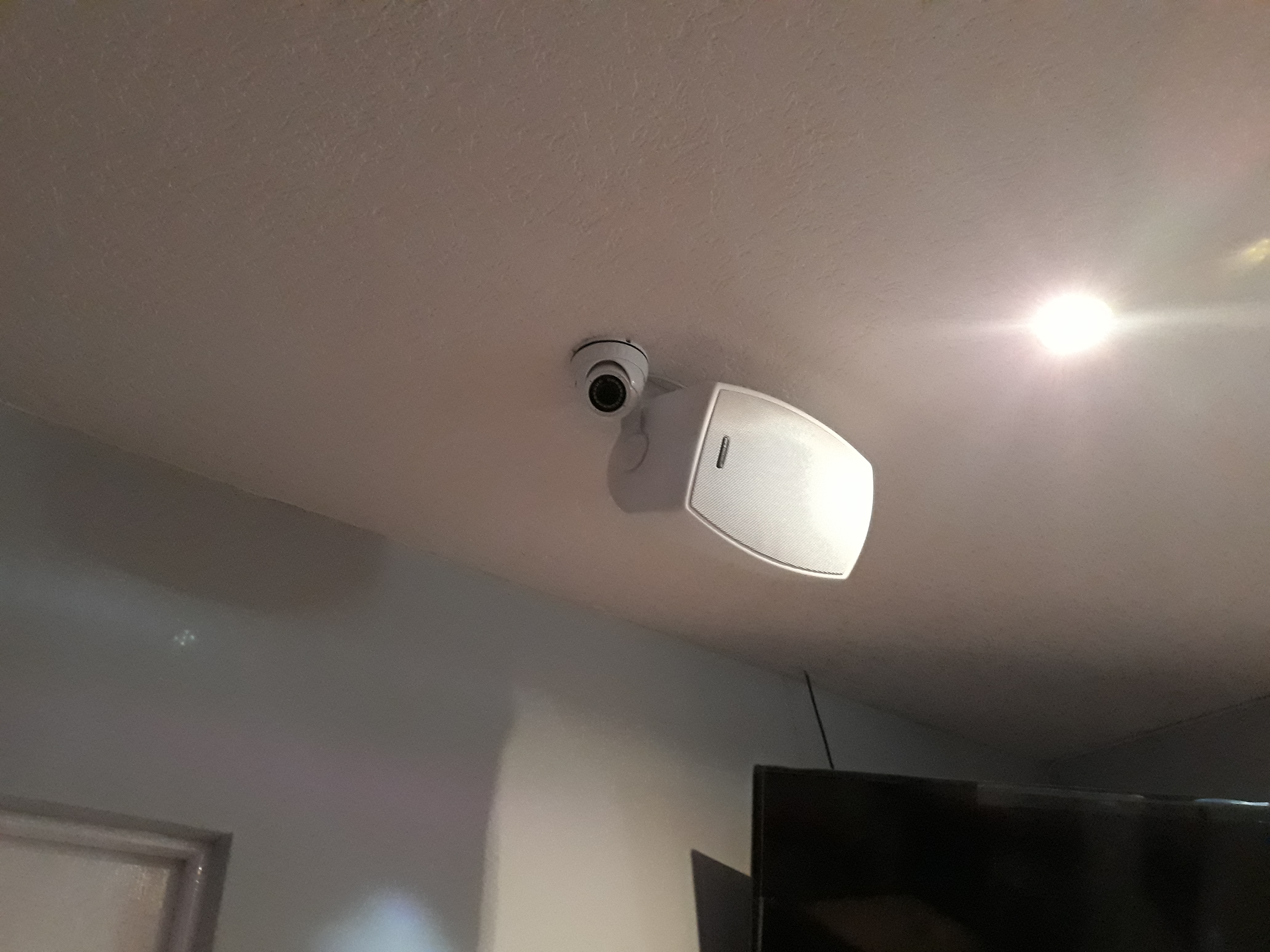 Kamera monitoringu i głośnik zamontowane na suficie w pomieszczeniu, widoczne przewody, ujęcie z dołu.