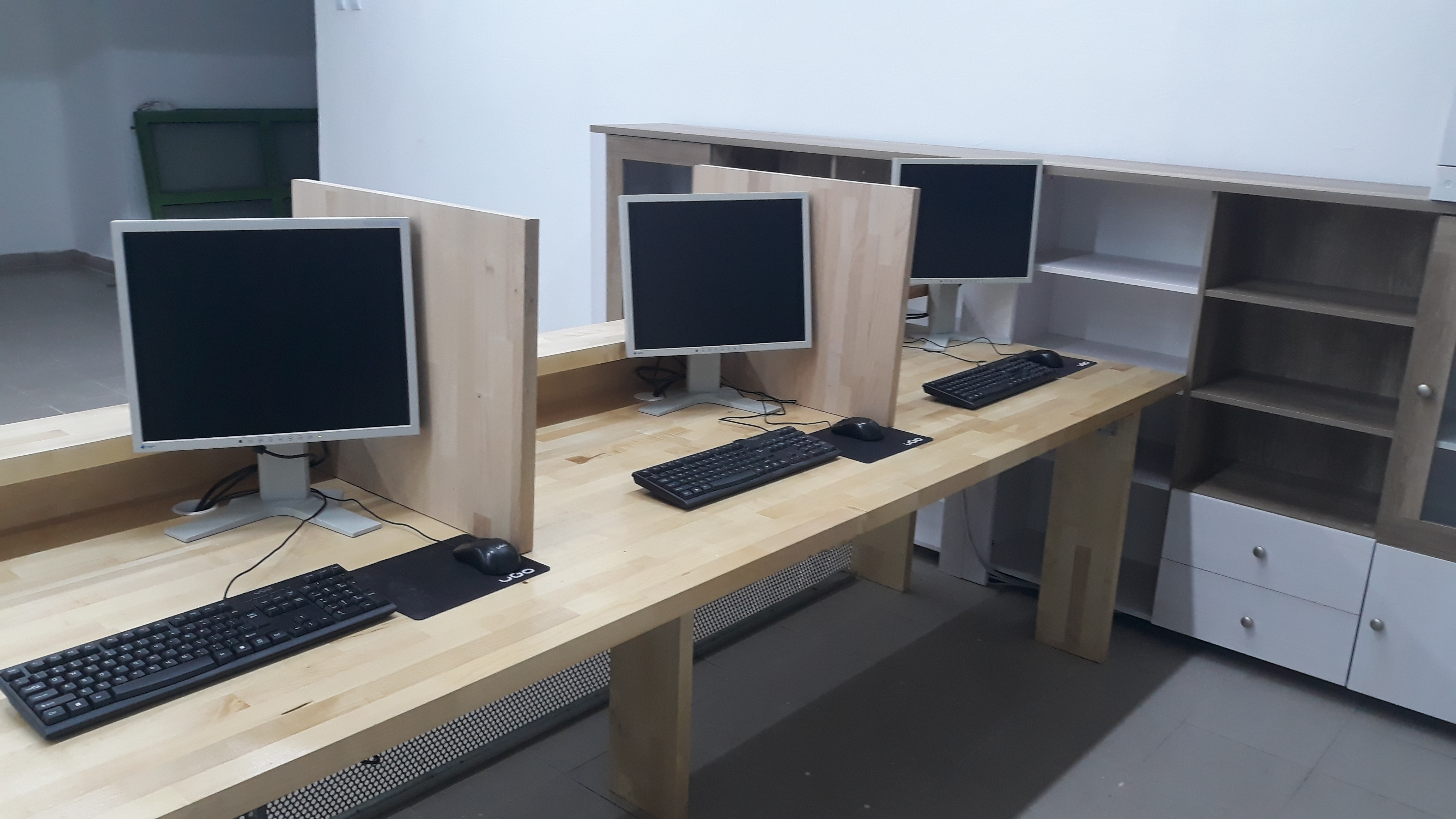 Stanowiska komputerowe z monitorami LCD, klawiaturami i myszkami na biurkach z przegrodami, ustawione w rzędzie w biurze.