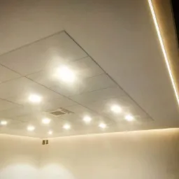 Sufit podwieszany z kwadratowymi panelami, oświetleniem punktowym i liniowym LED wzdłuż krawędzi, widoczny fragment klimatyzacji, ujęcie z dołu.