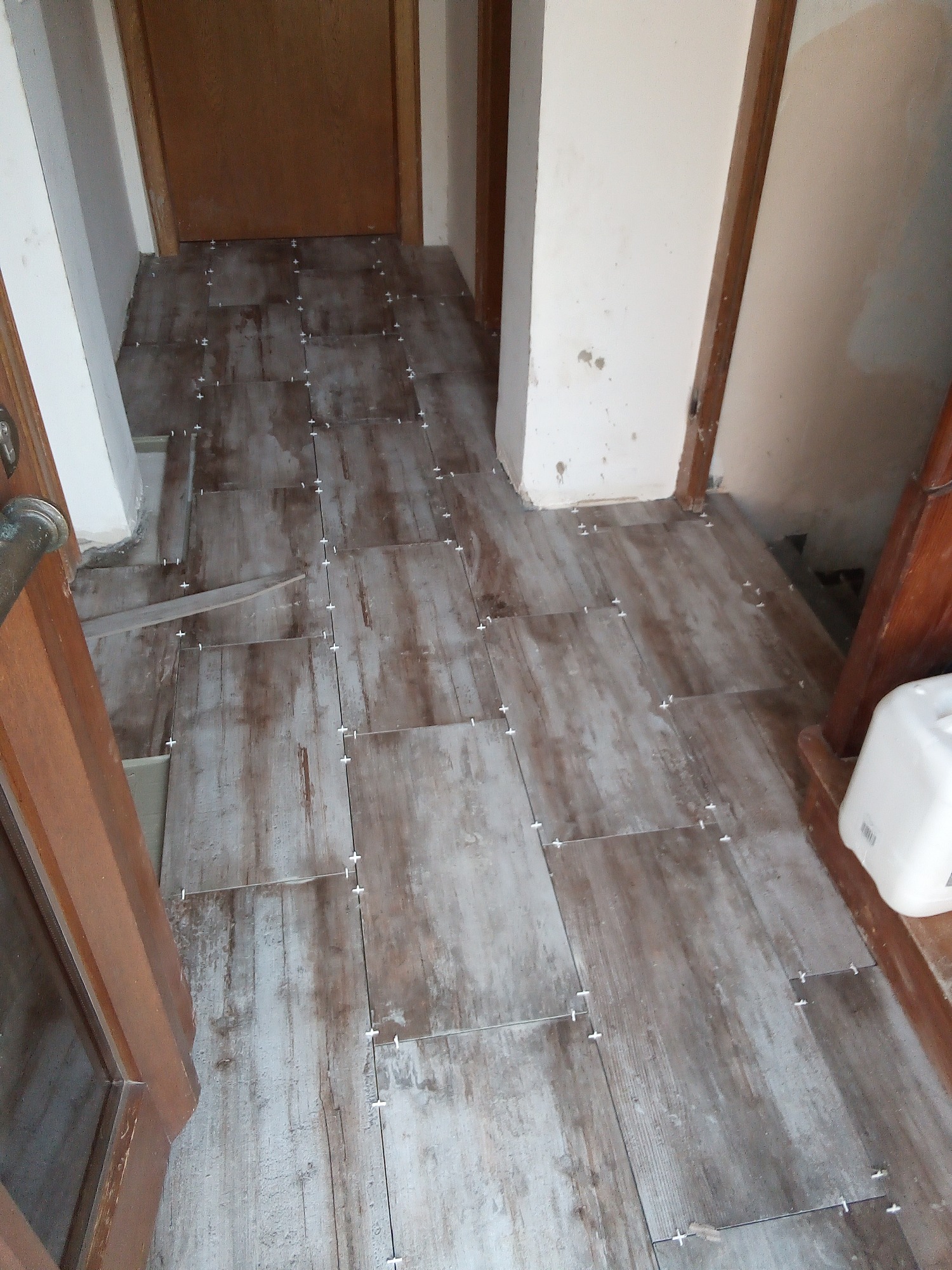 Układanie płytek podłogowych imitujących drewno w korytarzu, widoczne krzyżyki dystansowe i niedokończone fugowanie.