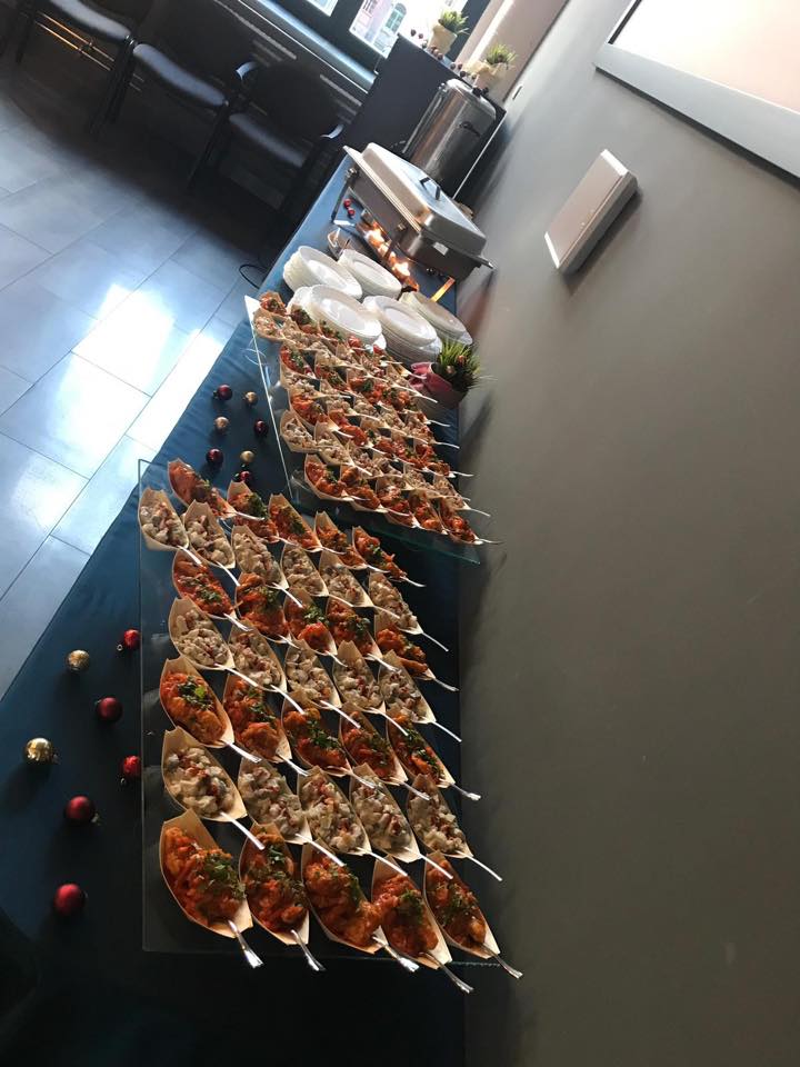 Ustawiony stół z rzędami przystawek w łódeczkach na srebrnych łyżeczkach, obok dekoracje świąteczne i podgrzewacz do potraw.