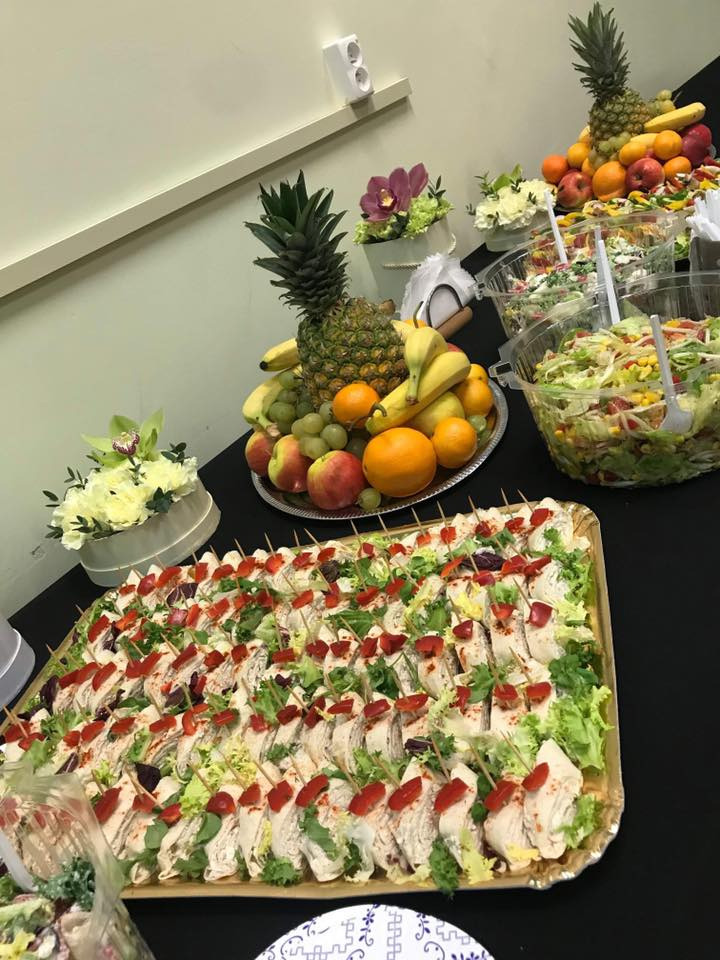 Stół z przekąskami: tortille z warzywami na złotej tacy, sałatki w przezroczystych miskach, owoce (ananas, banany, pomarańcze, jabłka) na srebrnej paterze, dekoracje kwiatowe.